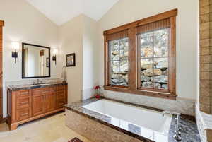 Bathroom featuring vanity, a bath, and lofted ceiling
