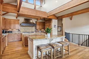 Two tone kitchen featuring a breakfast bar area, two tone cabinetry, light wood-type flooring, lofted ceiling, and light stone counters