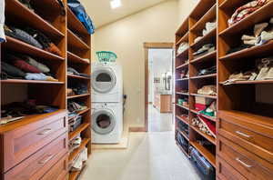 Laundry area with light colored carpet, stacked washer and clothes dryer, and vaulted ceiling