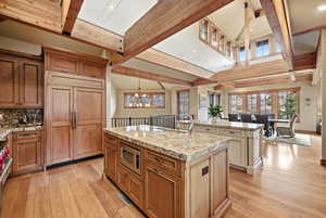 Kitchen featuring beamed ceiling, light stone countertops, light wood-style flooring, built in appliances, and suspended lighting