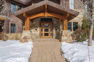 Snow covered property entrance with stone siding and covered porch