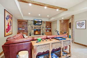 Living room featuring light carpet, a raised ceiling, a stone fireplace, recessed lighting, and beam ceiling