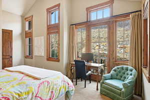 Bedroom featuring lofted ceiling, light carpet, and a desk