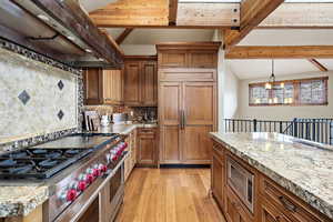 Kitchen with built in appliances, exhaust hood, vaulted ceiling with beams, wood finish cabinetry, and light wood-type flooring