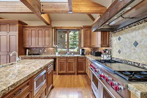 Kitchen with extractor fan, stainless steel appliances, wood finish cabinetry, light wood-style floors, and light stone counters