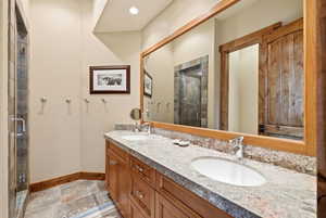 Bathroom with double vanity, light stone finish floors, and a stall shower