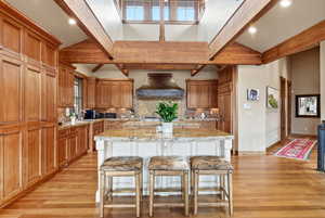 Dual tone kitchen featuring light stone countertops, a kitchen island with sink, a kitchen breakfast bar, backsplash, and recessed lighting