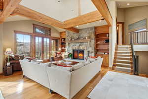 Living area featuring built in features, light wood-style floors, french doors, a stone fireplace, and lofted ceiling