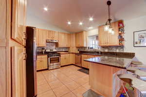 Kitchen with lofted ceiling, a peninsula, a breakfast bar area, stainless steel appliances, and light wood finish cabinetry