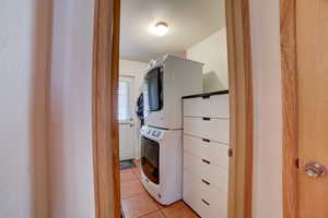 Laundry room featuring light tile patterned floors, stacked washer and clothes dryer, and a textured ceiling