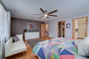 Bedroom with light wood-type flooring, ensuite bath, a walk in closet, and a ceiling fan