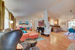 Living area featuring lofted ceiling, healthy amount of natural light, light wood-type flooring, and a chandelier