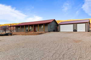 View of front of house with a metal roof, covered porch, an outdoor structure, driveway, and a garage