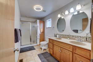 Bathroom with double vanity, a shower stall, light tile patterned floors, and backsplash