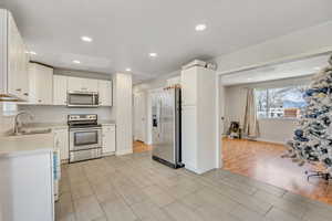 Kitchen with stainless steel appliances, light countertops, white cabinetry, wood tiled floors, and recessed lighting
