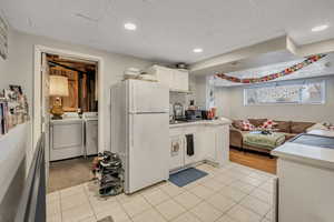 Kitchen featuring freestanding refrigerator, light countertops, white cabinetry, a drop ceiling, and independent washer and dryer