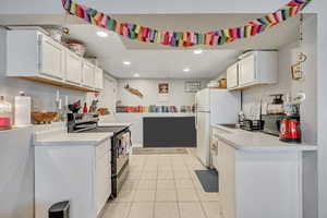 Kitchen featuring white cabinets, black / electric stove, light countertops, light tile patterned floors, and freestanding refrigerator