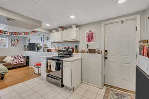 Kitchen with electric range, white cabinetry, light countertops, open floor plan, and light tile patterned flooring