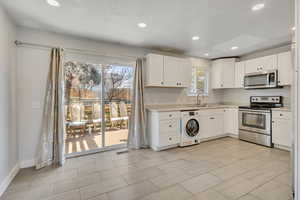Kitchen featuring stainless steel appliances, white cabinetry, light countertops, washer / clothes dryer, and recessed lighting