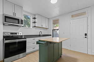 Dual tone kitchen with butcher block countertops, stainless steel appliances, healthy amount of natural light, light wood-type flooring, and two tone color scheme