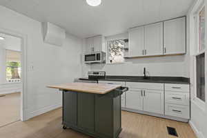 Kitchen featuring wooden counters, light wood-style floors, stainless steel appliances, a center island, and a breakfast bar area