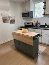 Two tone kitchen with stainless steel appliances, a kitchen island, wood counters, light wood-type flooring, and two tone cabinets