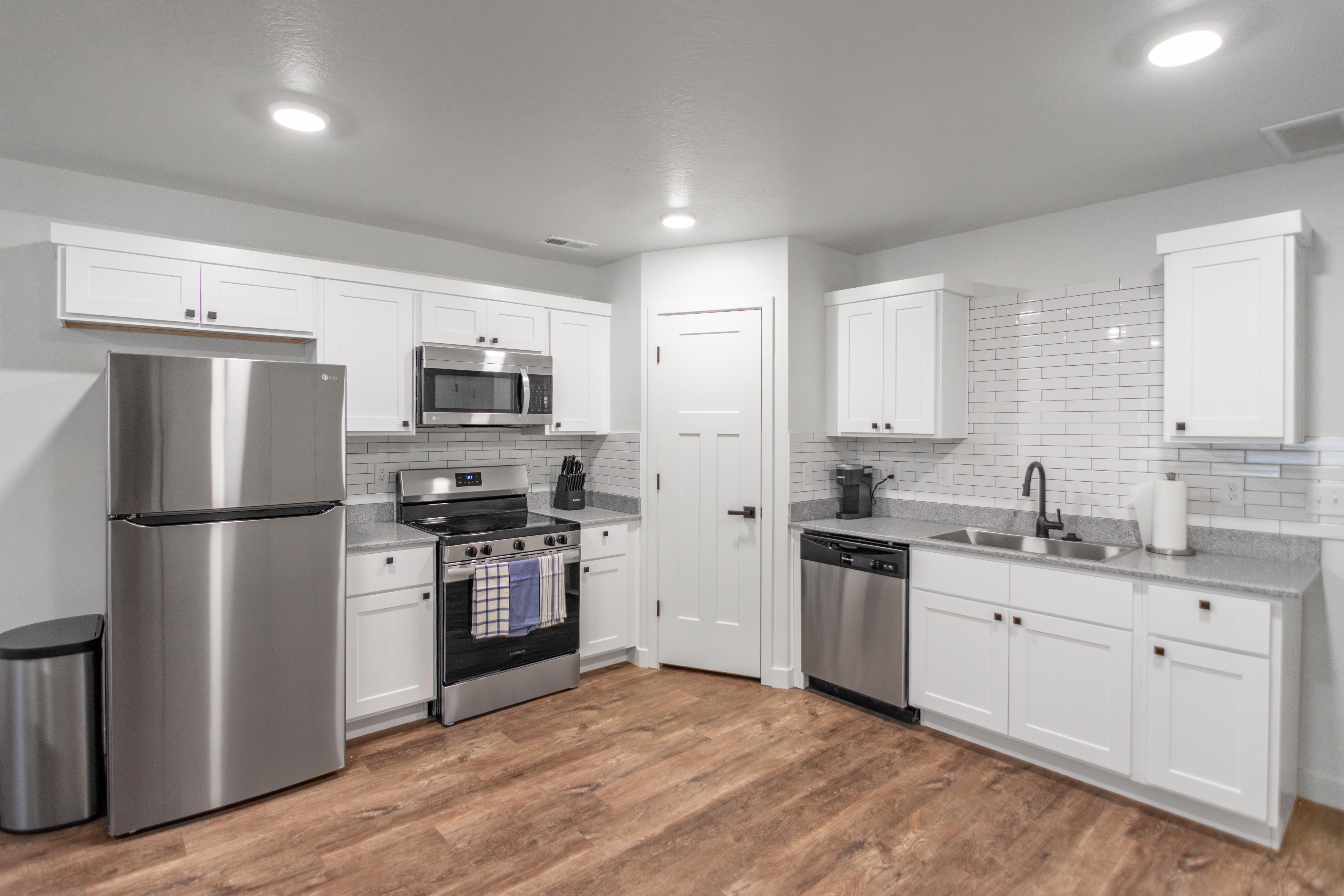 Kitchen with stainless steel appliances, white cabinets, dark wood finished floors, tasteful backsplash, and light stone countertops