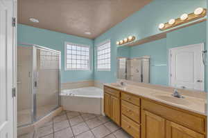 Full bathroom featuring double vanity, light tile patterned floors, a stall shower, a garden tub, and a textured ceiling