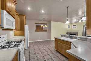 Kitchen featuring white appliances, a fireplace, wood finish cabinetry, light countertops, and a textured ceiling