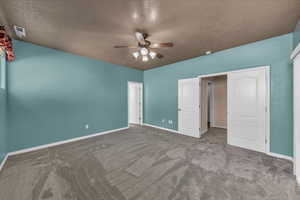 Unfurnished bedroom with a textured ceiling, dark carpet, and ceiling fan