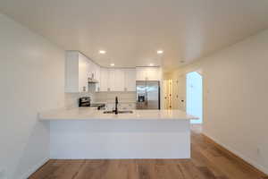 Kitchen featuring white cabinetry, stainless steel appliances, a peninsula, light wood-type flooring, and recessed lighting