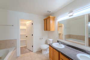 Bathroom featuring a bath, a walk in closet, light tile patterned flooring, and double vanity