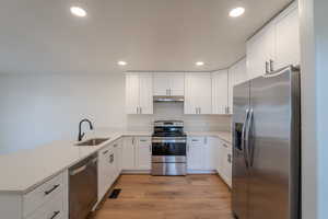 Kitchen with stainless steel appliances, white cabinetry, a peninsula, recessed lighting, and light wood-type flooring