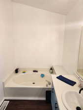 Full bath with vanity, a garden tub, and dark wood finished floors
