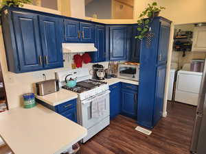 Kitchen featuring stainless steel appliances, blue cabinetry, light countertops, separate washer and dryer, and dark wood-style floors