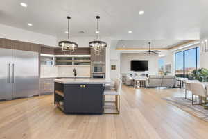 Two tone kitchen with suspended lighting, stainless steel appliances, a kitchen bar, a kitchen island, and light stone countertops