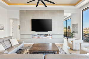 Living area featuring light wood-type flooring, ceiling fan, and a raised ceiling
