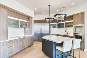 Kitchen featuring glass fronted cabinets, a center island, stainless steel appliances, a kitchen breakfast bar, and light wood finished floors
