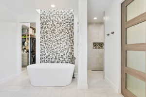 Full bathroom featuring tile walls, stacked washer and dryer, a soaking tub, light tile patterned floors, and recessed lighting