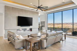 Living area with ceiling fan, light wood finished floors, a raised ceiling, a tiled fireplace, and recessed lighting