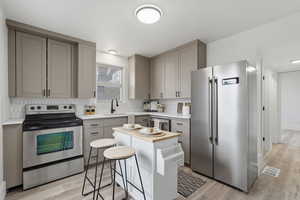 Kitchen featuring gray cabinets, stainless steel appliances, light wood finished floors, and backsplash