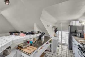 Kitchen with vaulted ceiling, stainless steel appliances, tile countertops, white cabinetry, and light tile patterned floors