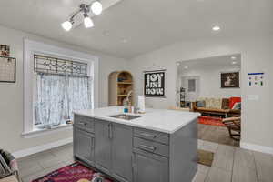 Kitchen with gray cabinetry, open floor plan, light stone counters, and lofted ceiling