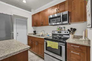 Kitchen featuring stainless steel appliances, wood finish cabinets, light countertops, ornamental molding, and light tile patterned floors