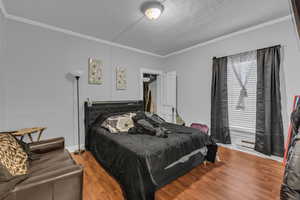 Bedroom with wood finished floors and ornamental molding