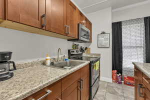 Kitchen with stainless steel appliances, wood finish cabinets, crown molding, and light stone countertops