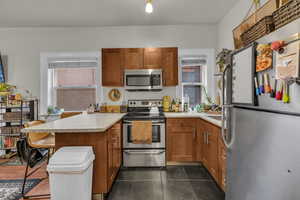 Kitchen with wood finish cabinetry, stainless steel appliances, a peninsula, a breakfast bar, and light countertops