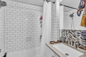 Bathroom featuring shower / bath combo with shower curtain, tasteful backsplash, and vanity