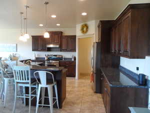 Kitchen with a kitchen breakfast bar, stainless steel appliances, hanging light fixtures, dark wood finish cabinetry, and dark stone counters