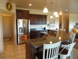 Kitchen with stainless steel refrigerator with ice dispenser, dark wood finish cabinetry, a kitchen breakfast bar, dark stone countertops, and an island with sink